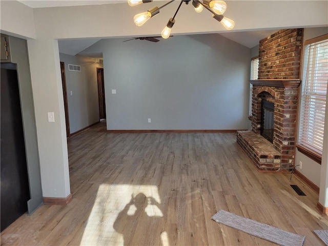 unfurnished living room featuring lofted ceiling, light wood-type flooring, ceiling fan with notable chandelier, and a brick fireplace