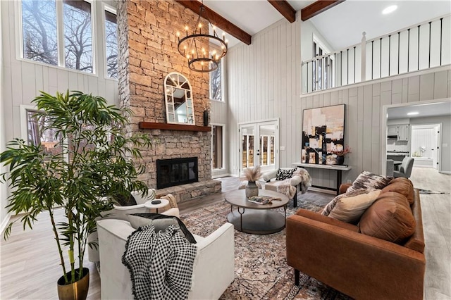 living room with a stone fireplace, a chandelier, light wood-type flooring, beam ceiling, and a high ceiling