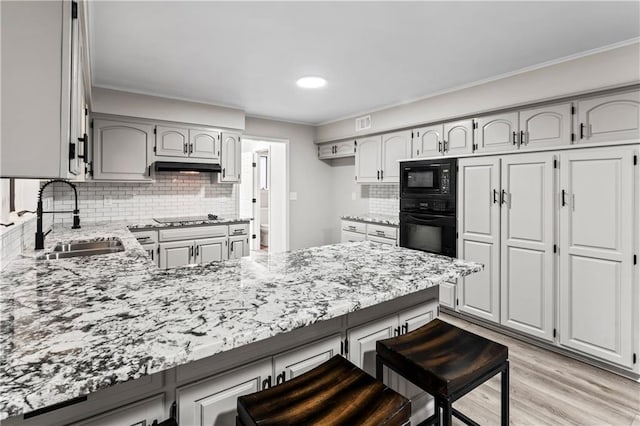 kitchen with sink, tasteful backsplash, black appliances, light hardwood / wood-style floors, and kitchen peninsula