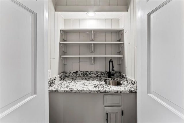 bar with light stone countertops, sink, and beam ceiling