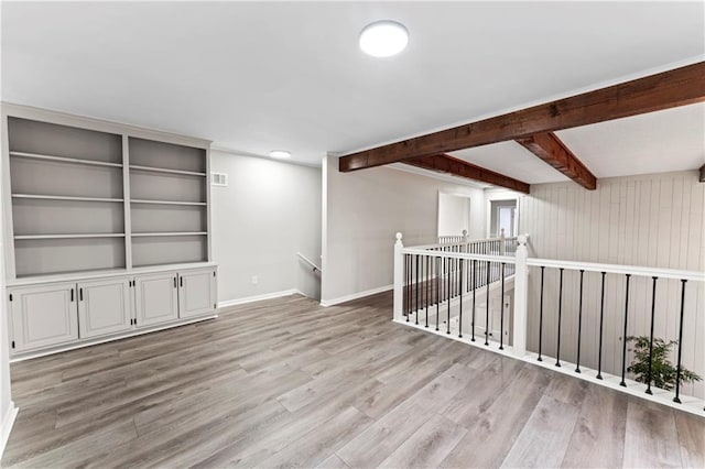 empty room featuring beam ceiling and light hardwood / wood-style flooring