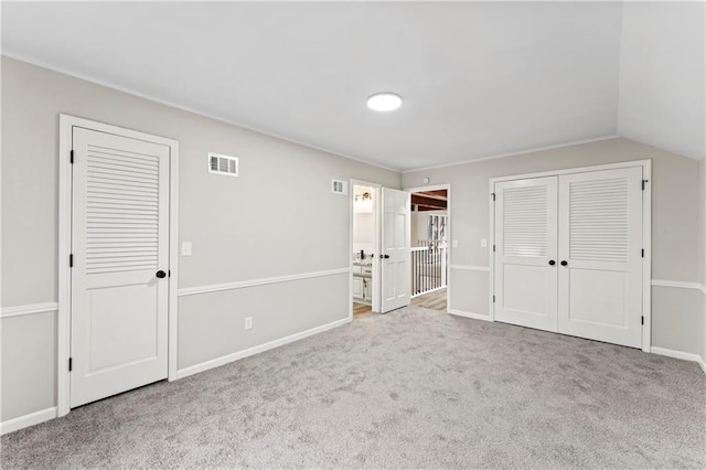 unfurnished bedroom featuring ensuite bathroom, vaulted ceiling, and light carpet