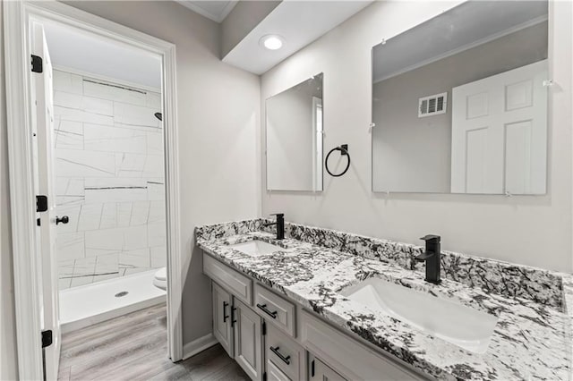 bathroom with hardwood / wood-style flooring, vanity, a tile shower, and toilet