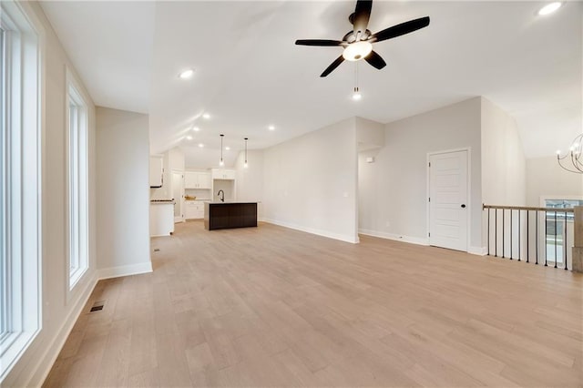 unfurnished living room with light wood finished floors, baseboards, vaulted ceiling, and ceiling fan with notable chandelier