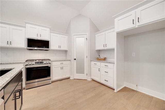 kitchen with light wood-style floors, backsplash, light stone counters, white cabinetry, and appliances with stainless steel finishes