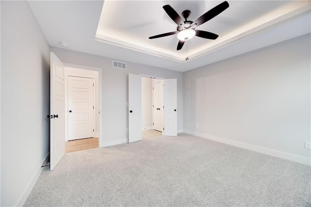 unfurnished bedroom featuring ceiling fan, a tray ceiling, visible vents, baseboards, and light colored carpet