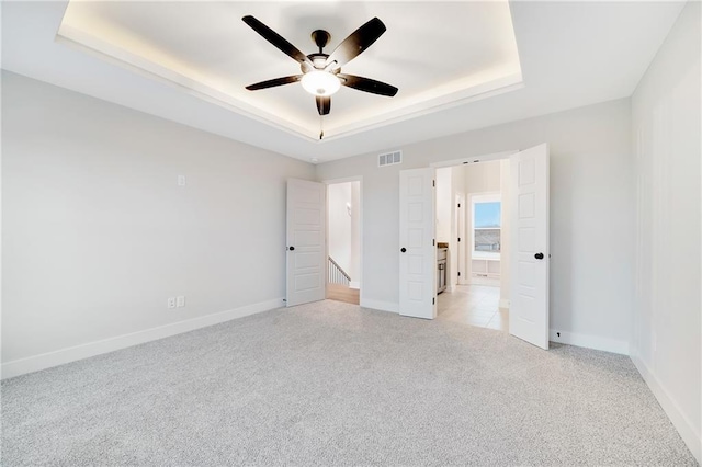 unfurnished bedroom featuring visible vents, light carpet, a raised ceiling, and baseboards