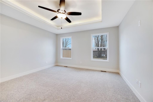 unfurnished room featuring visible vents, ceiling fan, light colored carpet, and a tray ceiling