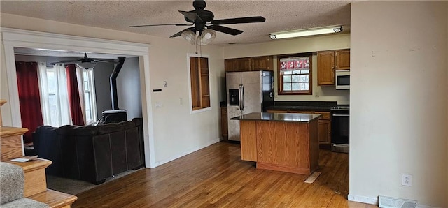 kitchen with a wood stove, appliances with stainless steel finishes, dark hardwood / wood-style floors, a kitchen island, and ceiling fan