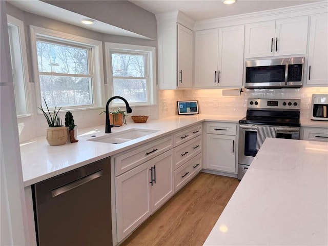 kitchen with decorative backsplash, appliances with stainless steel finishes, sink, white cabinets, and light hardwood / wood-style floors