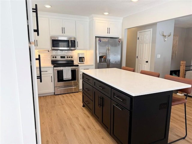 kitchen featuring white cabinets, a kitchen breakfast bar, a kitchen island, appliances with stainless steel finishes, and light hardwood / wood-style floors