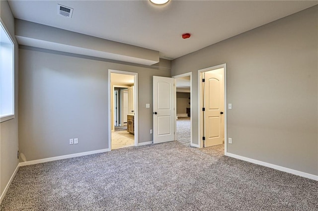 unfurnished bedroom with carpet flooring, ensuite bathroom, baseboards, and visible vents