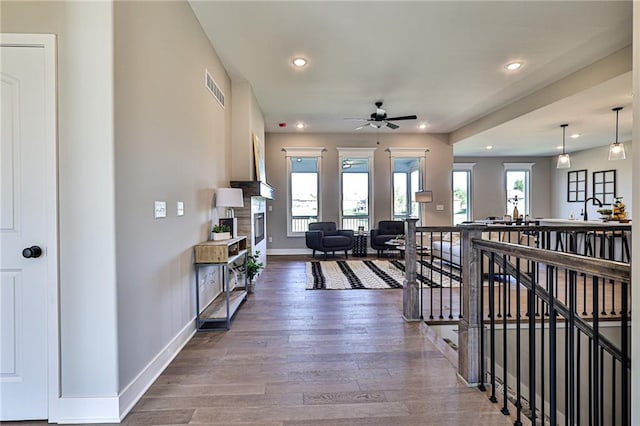 interior space with a ceiling fan, a fireplace, wood finished floors, baseboards, and visible vents