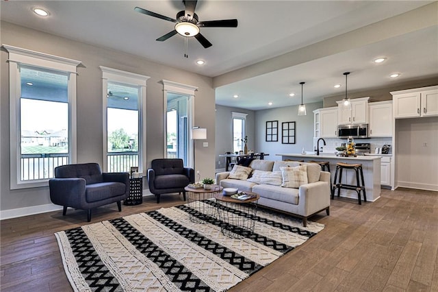 living area with baseboards, dark wood-style floors, a healthy amount of sunlight, and ceiling fan
