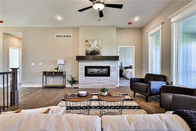 living area featuring baseboards, ceiling fan, visible vents, a fireplace, and wood finished floors