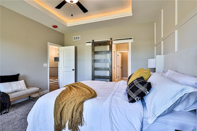 bedroom with carpet, a raised ceiling, a barn door, visible vents, and a ceiling fan