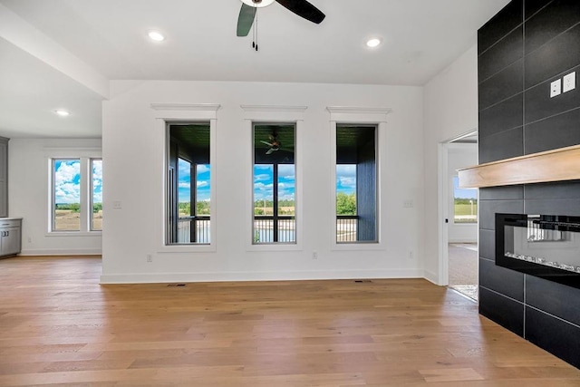 unfurnished living room featuring ceiling fan, light wood-type flooring, and a tiled fireplace