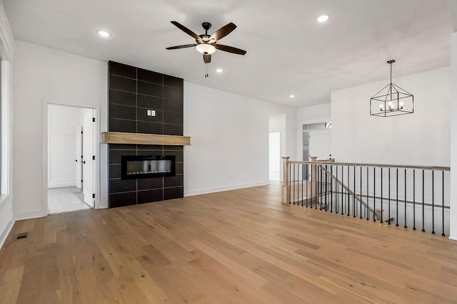 unfurnished living room with a tile fireplace, ceiling fan with notable chandelier, and light hardwood / wood-style floors