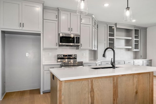 kitchen with stainless steel appliances, a kitchen island with sink, sink, decorative light fixtures, and light hardwood / wood-style floors