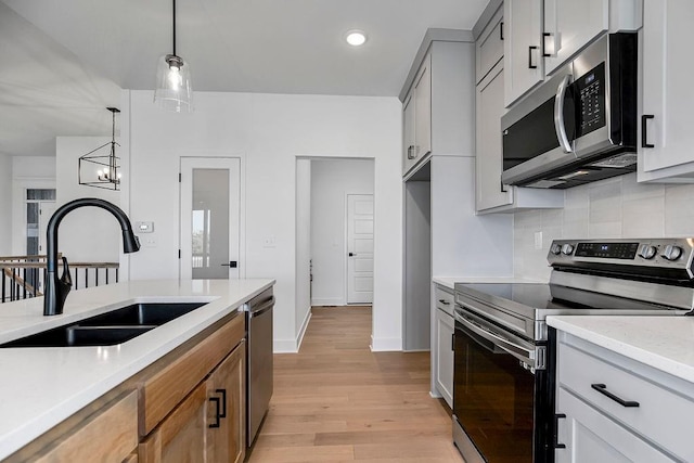 kitchen with sink, decorative light fixtures, light wood-type flooring, a notable chandelier, and stainless steel appliances