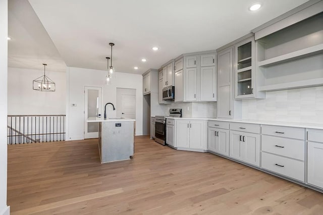 kitchen featuring sink, light wood-type flooring, tasteful backsplash, decorative light fixtures, and stainless steel appliances