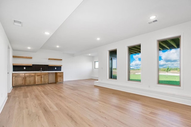 unfurnished living room featuring built in desk, light hardwood / wood-style floors, and sink