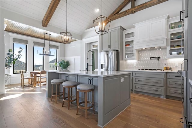 kitchen with decorative light fixtures, gray cabinets, a center island with sink, a kitchen bar, and stainless steel fridge with ice dispenser