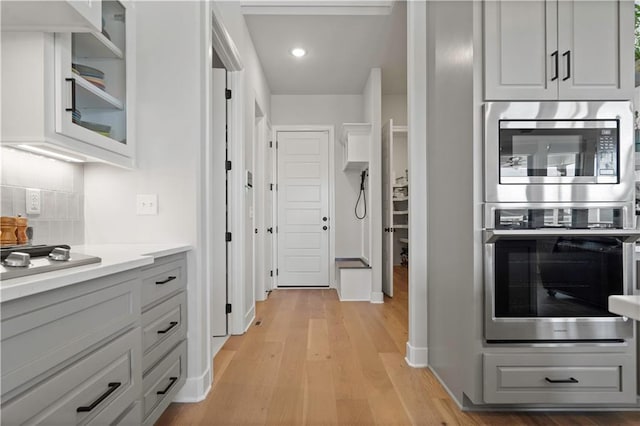 kitchen with tasteful backsplash, stainless steel double oven, gray cabinets, and light hardwood / wood-style floors