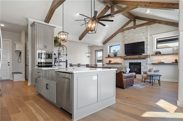 kitchen featuring pendant lighting, appliances with stainless steel finishes, a fireplace, gray cabinets, and a kitchen island with sink