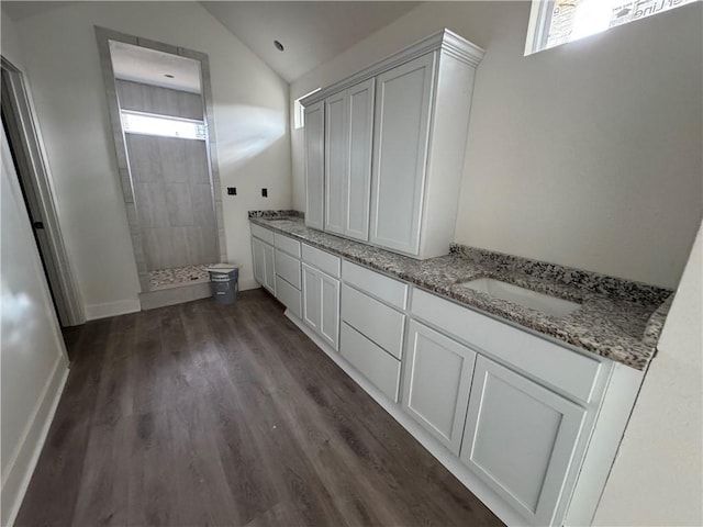 bathroom featuring hardwood / wood-style floors, vanity, a tile shower, and lofted ceiling