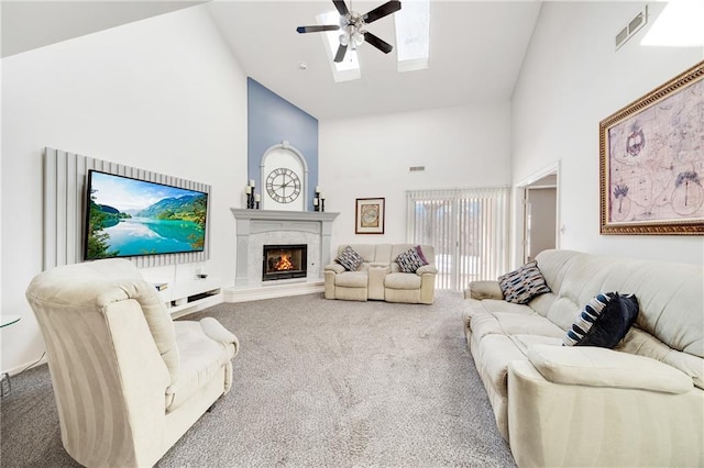 living room featuring high vaulted ceiling, a skylight, carpet flooring, ceiling fan, and a high end fireplace