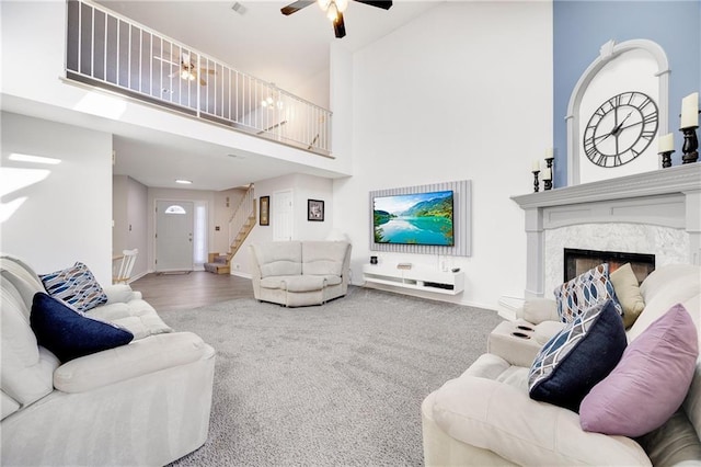 carpeted living room featuring a high end fireplace, ceiling fan, and a high ceiling