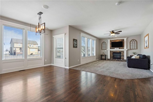 unfurnished living room featuring a stone fireplace, ceiling fan with notable chandelier, and dark hardwood / wood-style floors