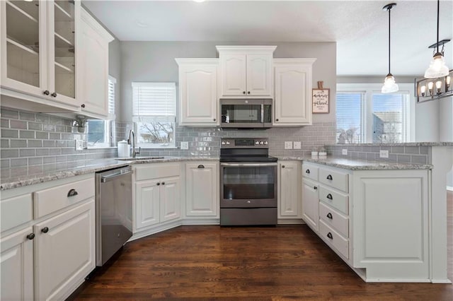 kitchen with stainless steel appliances, dark wood-type flooring, white cabinets, and decorative light fixtures