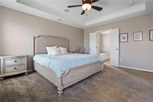 bedroom with a raised ceiling, dark carpet, ceiling fan, and ensuite bath