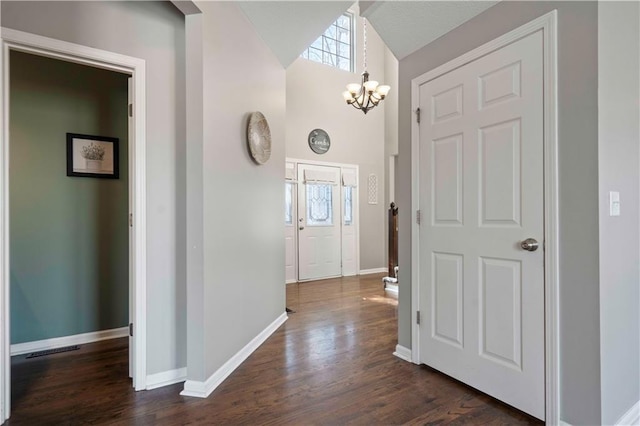 foyer entrance with dark wood-type flooring, vaulted ceiling, and a chandelier