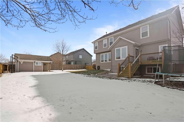 snow covered house with a garage, an outdoor structure, and a trampoline