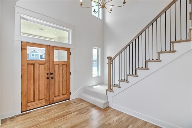 entrance foyer with plenty of natural light, light wood-type flooring, a towering ceiling, and a chandelier