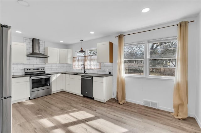 kitchen featuring sink, white cabinetry, stainless steel appliances, decorative light fixtures, and wall chimney exhaust hood