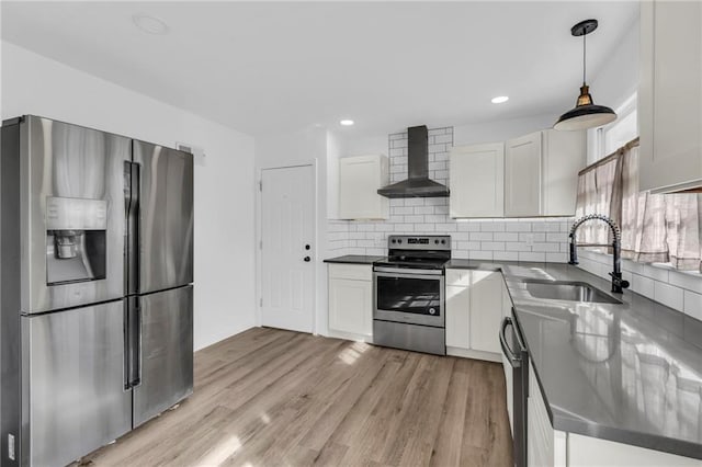 kitchen with sink, appliances with stainless steel finishes, white cabinets, decorative light fixtures, and wall chimney exhaust hood