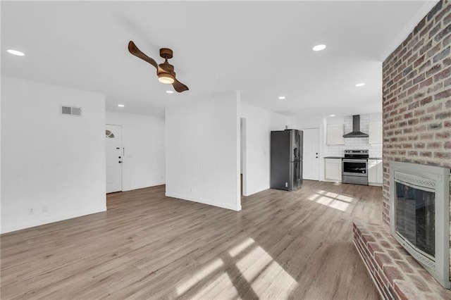 unfurnished living room featuring ceiling fan, a fireplace, and light wood-type flooring