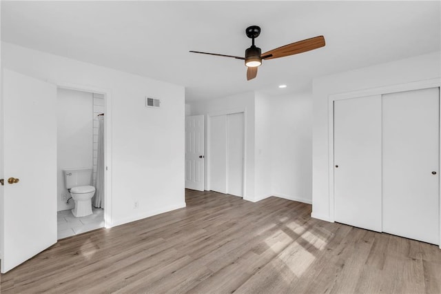 unfurnished bedroom featuring ceiling fan, two closets, light hardwood / wood-style floors, and ensuite bath