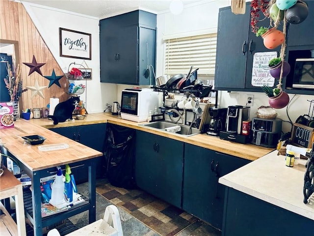 kitchen with blue cabinetry, butcher block counters, sink, and wooden walls