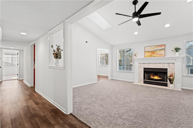 unfurnished living room featuring ceiling fan, a high end fireplace, plenty of natural light, and lofted ceiling with skylight