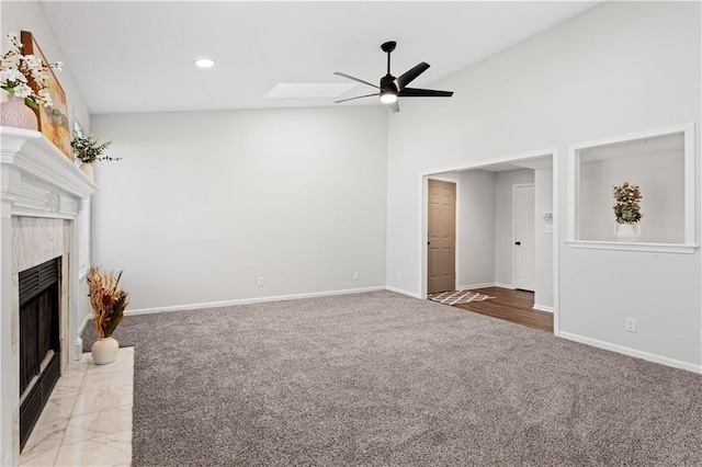 unfurnished living room with ceiling fan, vaulted ceiling with skylight, a high end fireplace, and light carpet