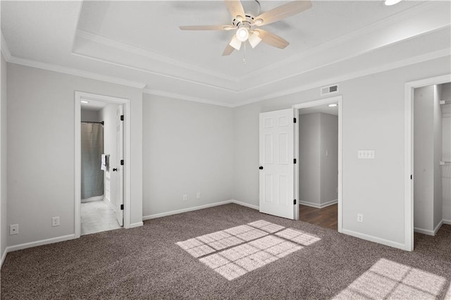 unfurnished bedroom featuring ceiling fan, ensuite bathroom, a tray ceiling, and dark colored carpet