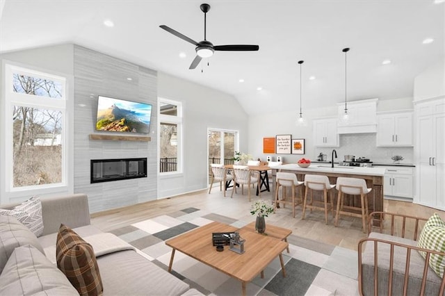 living room featuring lofted ceiling, sink, light hardwood / wood-style flooring, ceiling fan, and a fireplace