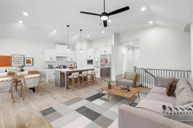 living room with light wood-type flooring, vaulted ceiling, ceiling fan, and sink