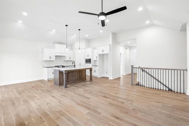 kitchen featuring pendant lighting, a center island with sink, sink, decorative backsplash, and white cabinetry