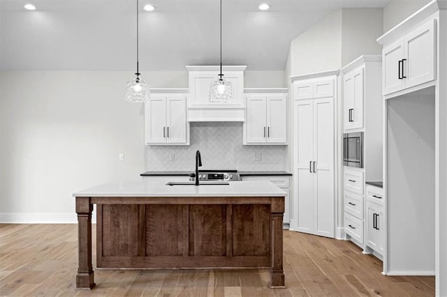 kitchen featuring a kitchen island with sink, white cabinets, and decorative light fixtures